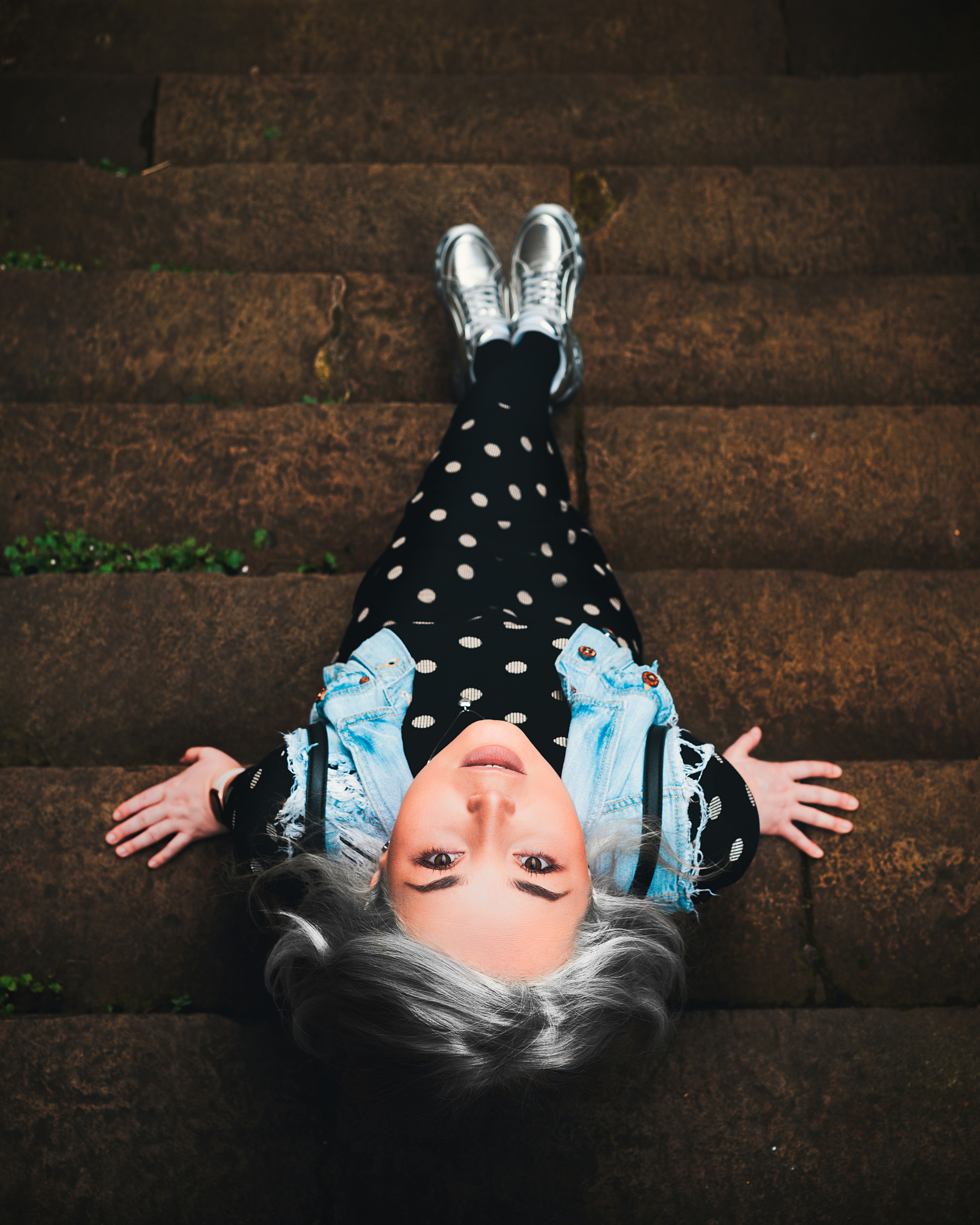 girl in black and white polka dot dress lying on brown concrete stairs
